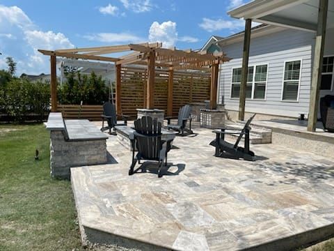 A patio with chairs and a pergola in front of a house.