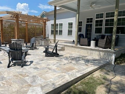 A patio with chairs and a pergola in front of a house.