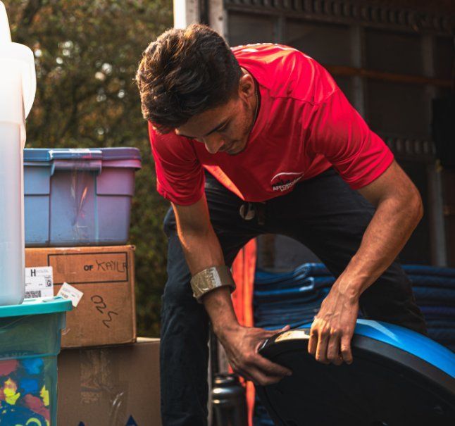Man in red shirt loads a truck, kneeling to handle a piece of blue furniture.