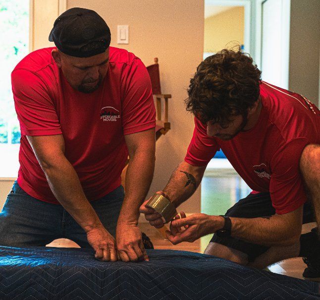 Two men in red shirts carefully wrap an object on a blue blanket.