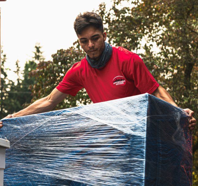 Man in red shirt lifting a large, wrapped box outdoors.
