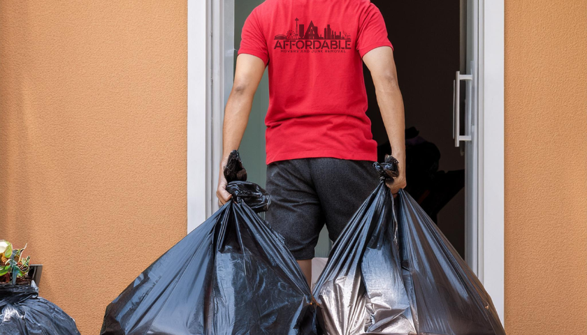 Affordable Mover's team member in red shirt carrying two black trash bags out a door.