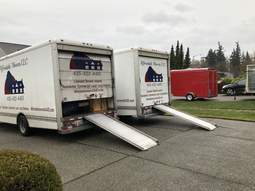 Two moving trucks with ramps extended, parked on a residential street.