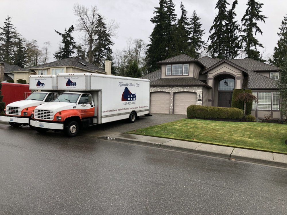 Moving trucks parked in front of a house, cloudy day.