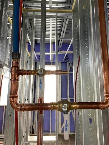 Plumbing pipes and fittings in a metal stud wall, with copper and blue pipes and ball valves.