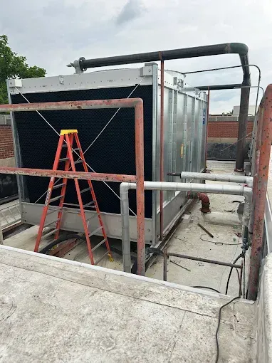 Cooling tower unit on a rooftop, with a red ladder leaned against it.