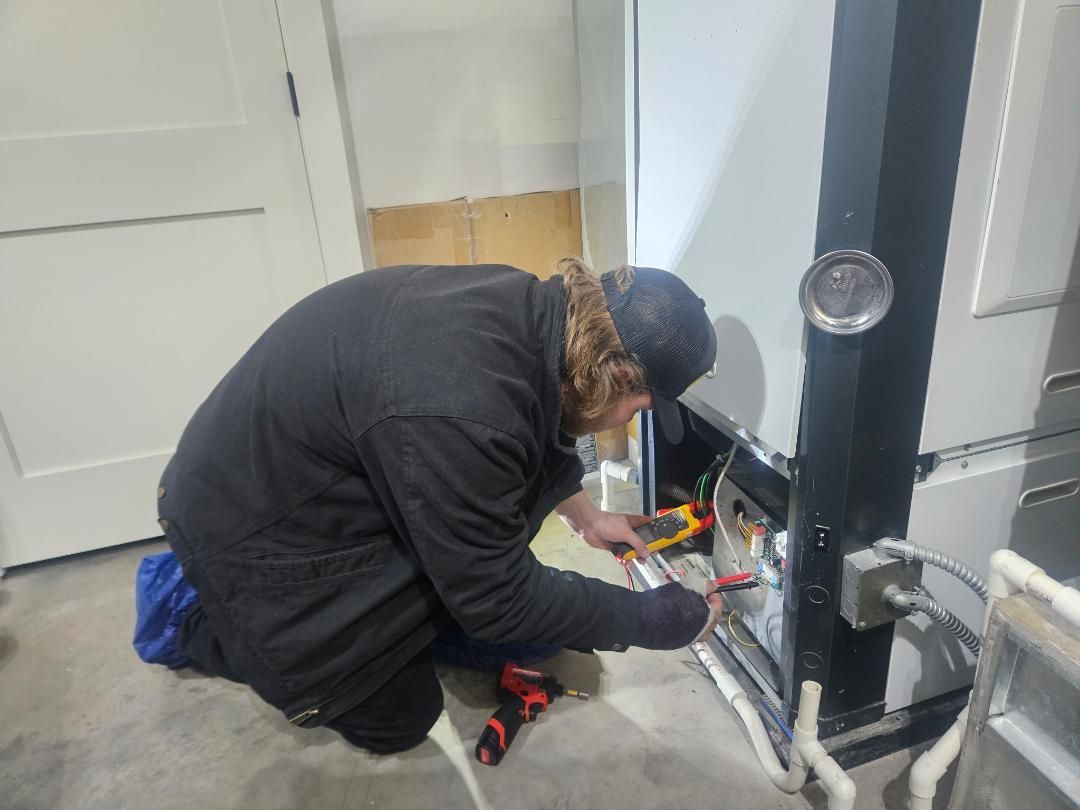 Technician inspecting electrical panel in a basement utility room, with exposed wiring and pipes.