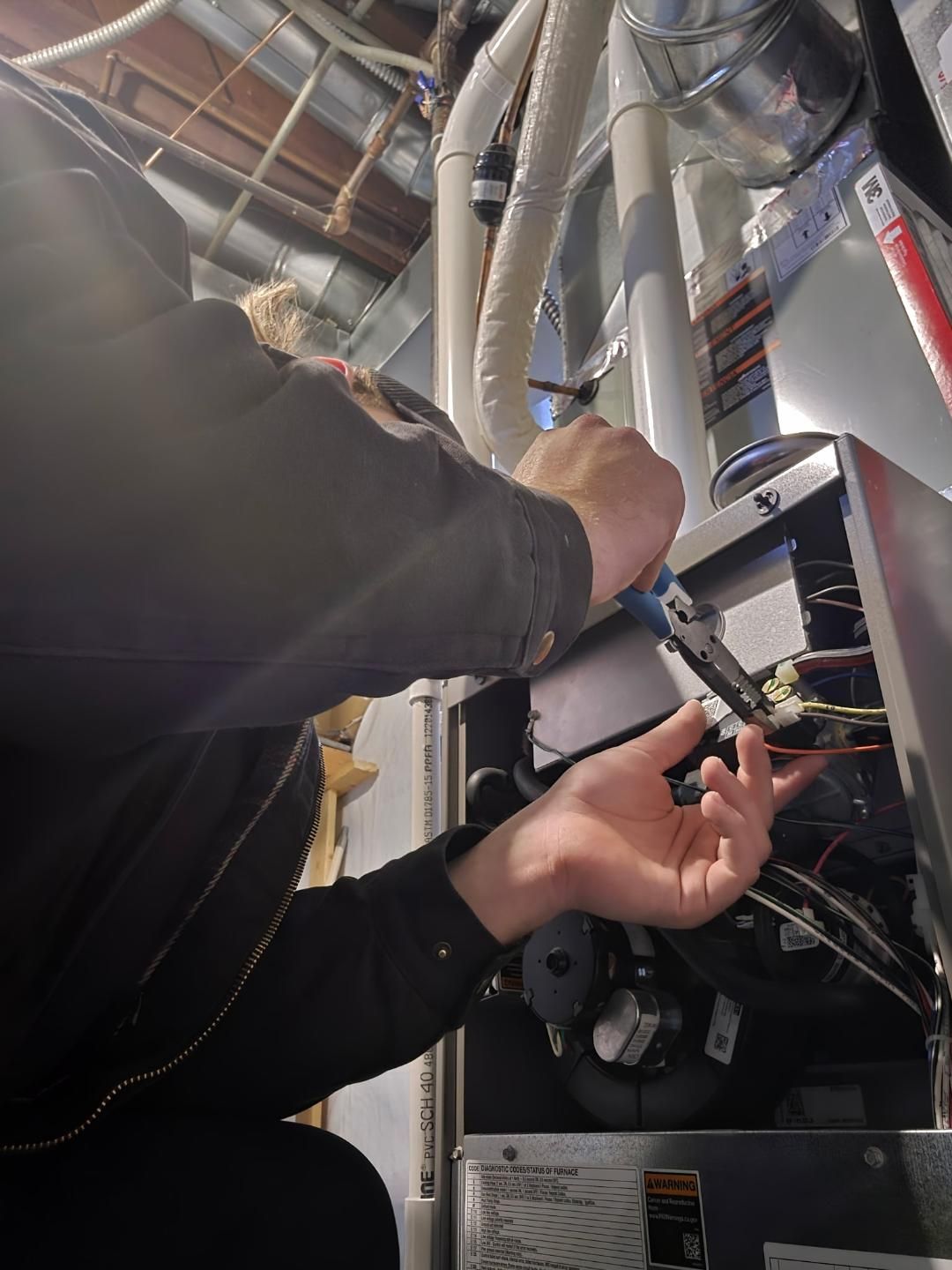Technician inspecting electrical panel in a basement utility room, with exposed wiring and pipes.