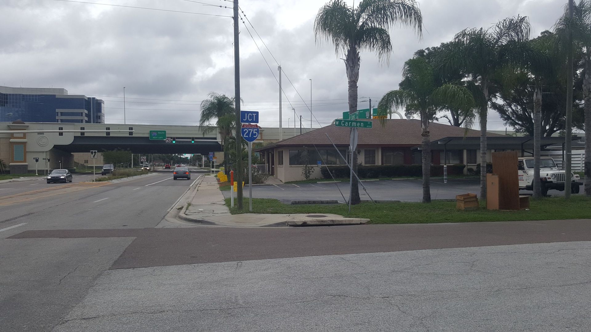 Empty parking lot with palm trees and an overcast sky near a low commercial building.