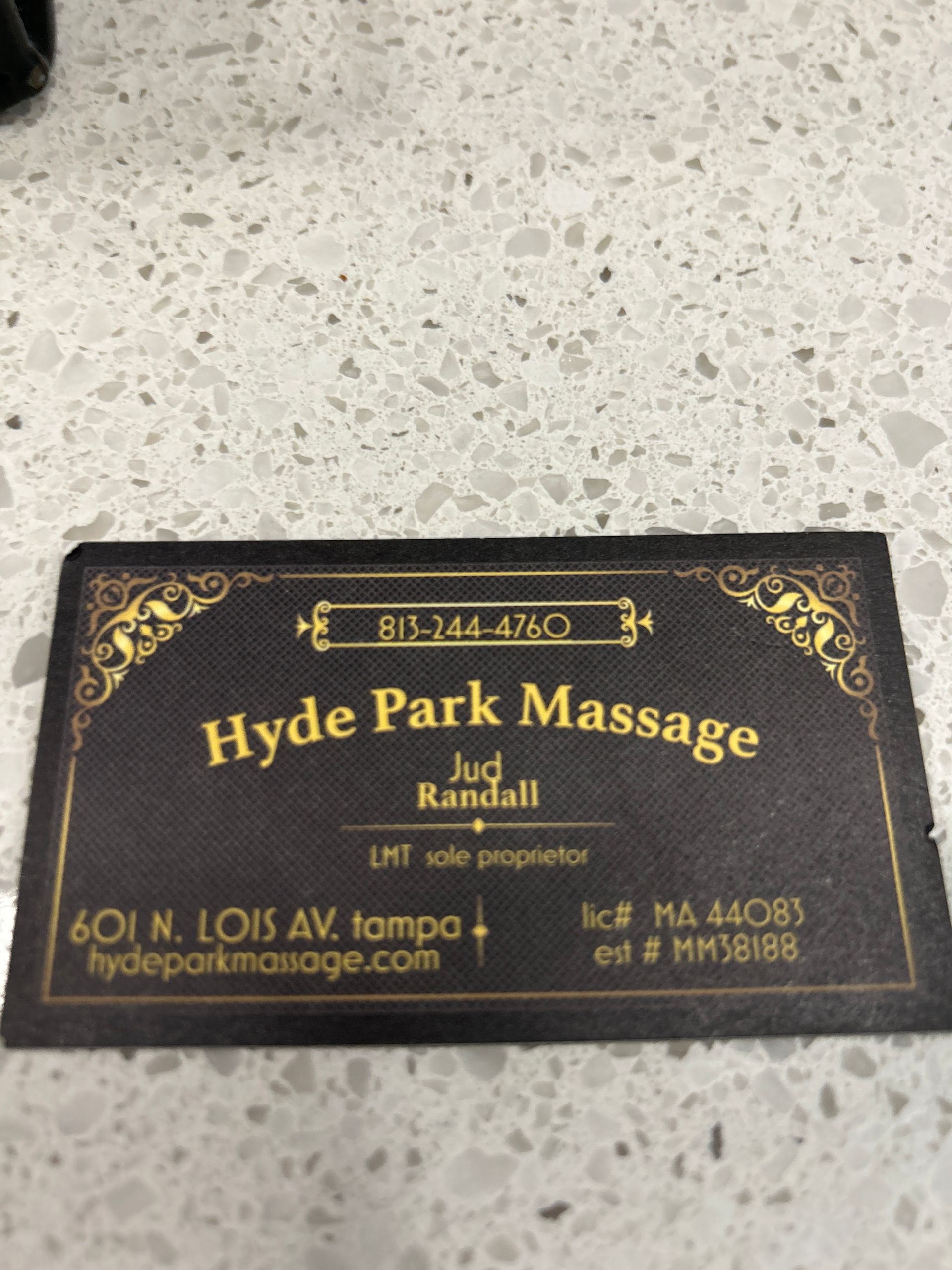 Black and gold Hyde Park Massage business card on a light speckled surface