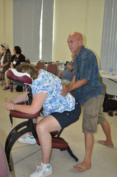 Massage therapy session in a classroom, with a man massaging a seated person on a chair.
