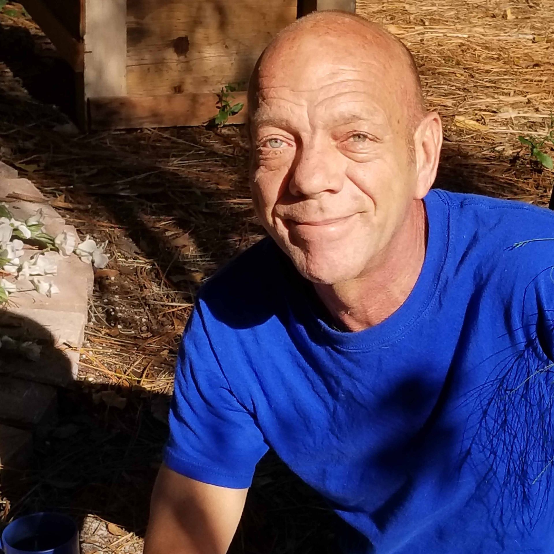 Smiling bald man in a bright blue shirt outdoors in warm sunlight