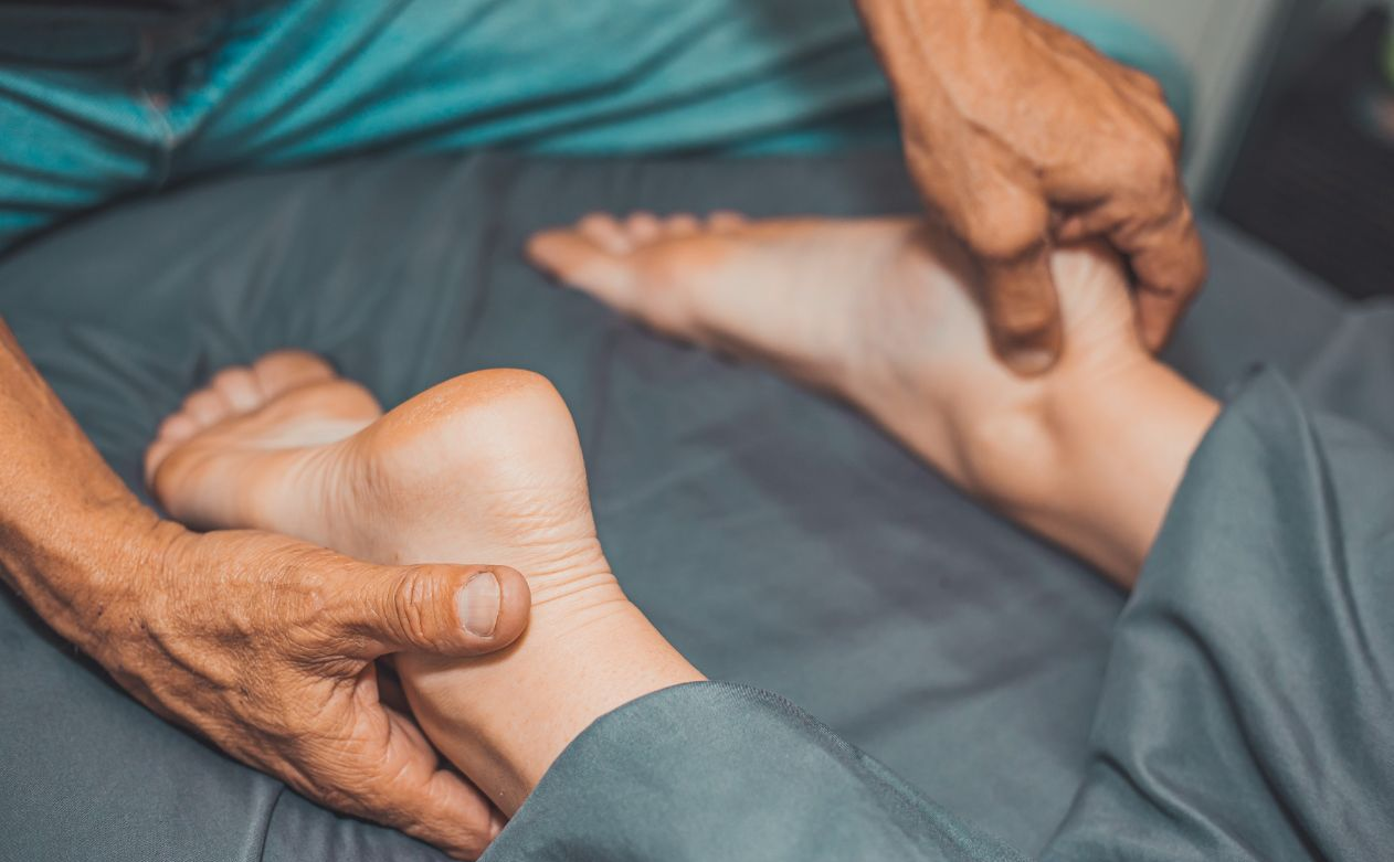 Hands holding a person’s feet during a massage on a bed with gray sheets.