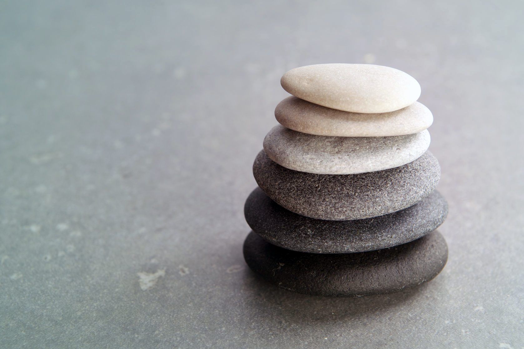 Stack of smooth pebbles in shades of white to dark gray on a gray surface
