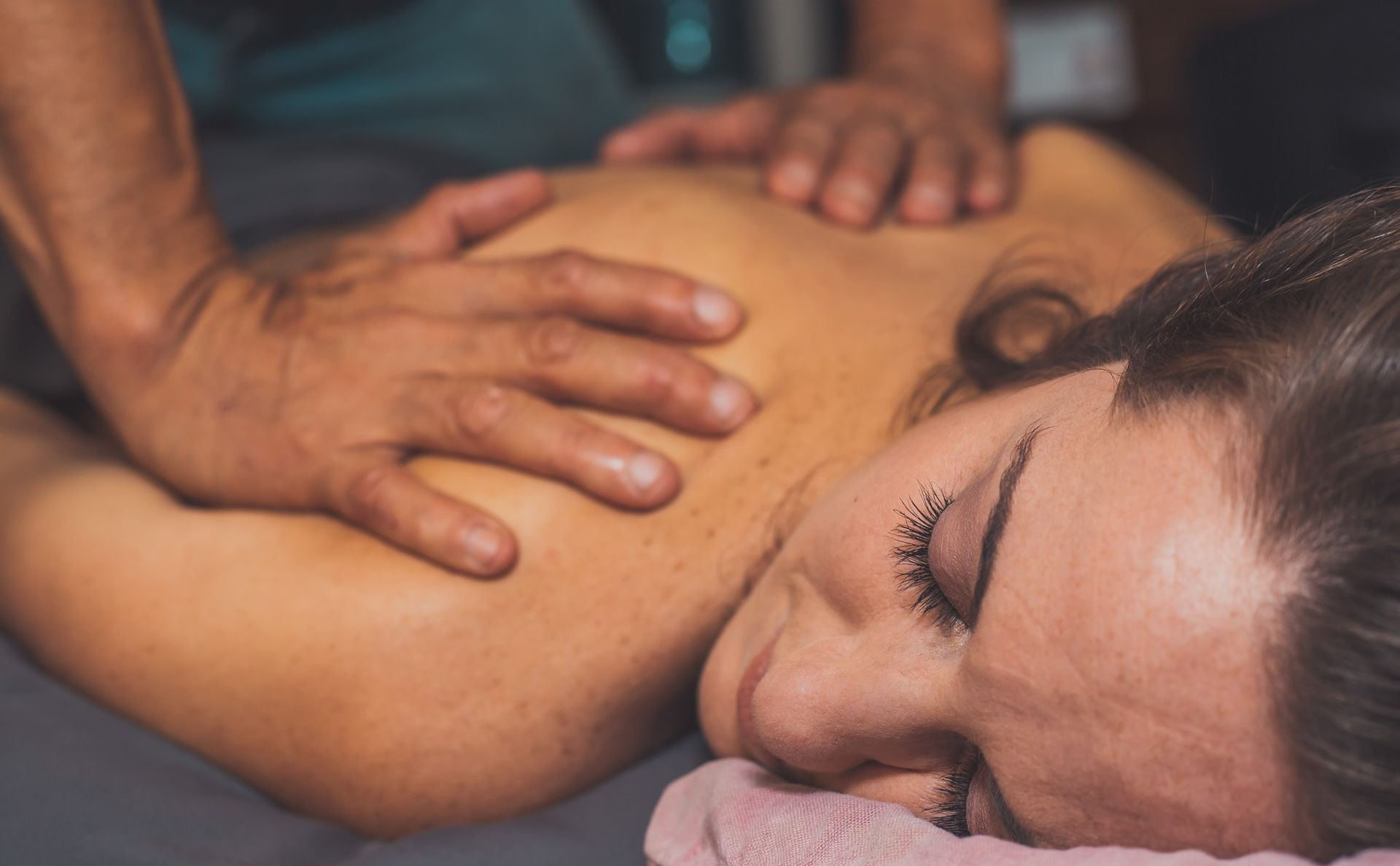 Massage therapist pressing shoulders of a relaxed person lying face down on a table