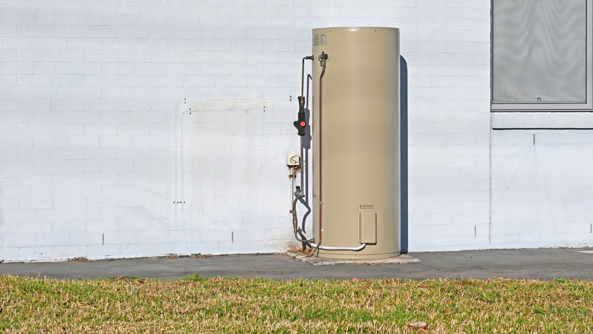 A tan water heater is sitting on the side of a white building.