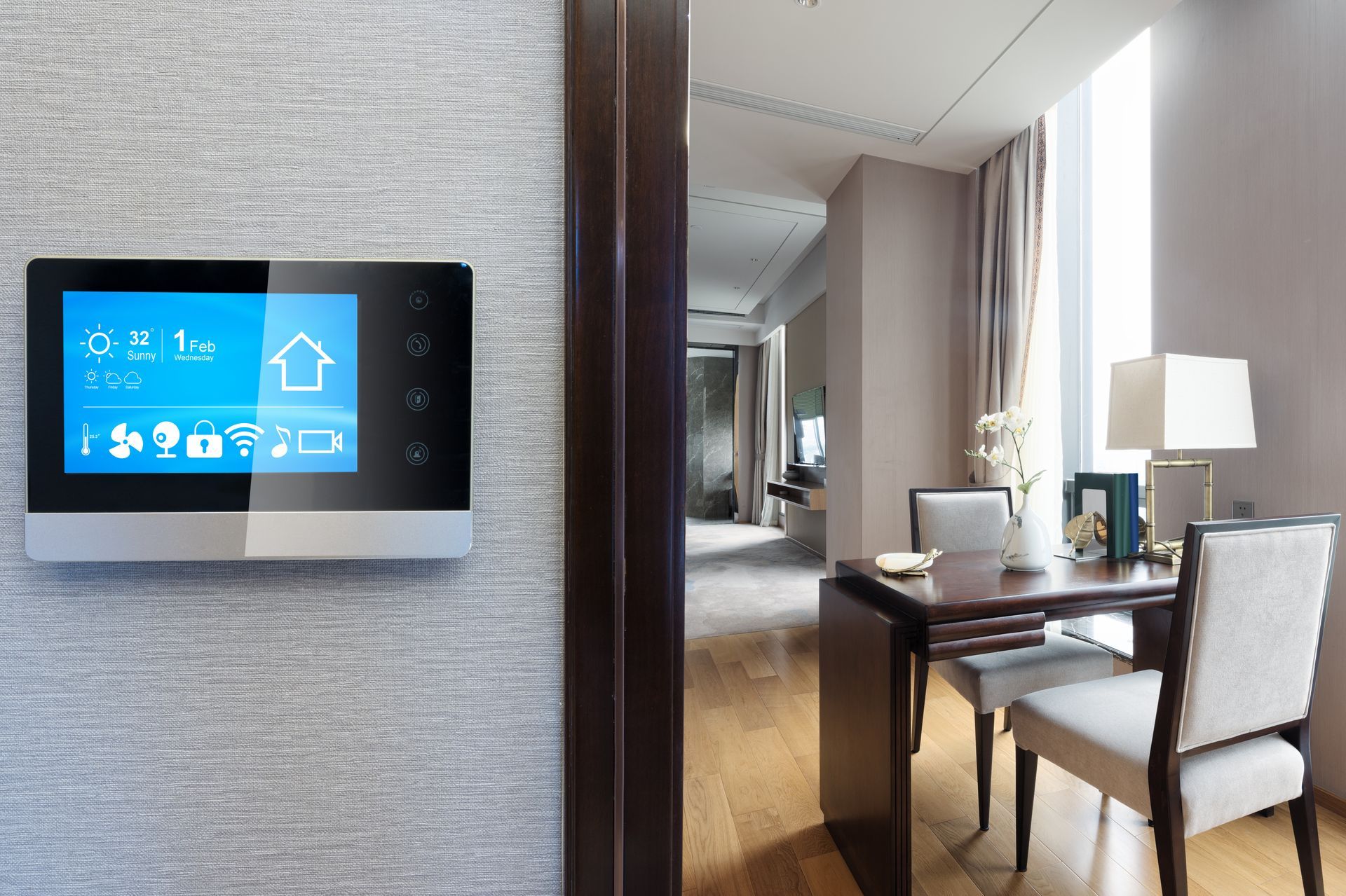 Smart home control panel on a textured wall, overlooking a dining area with a table and chairs.