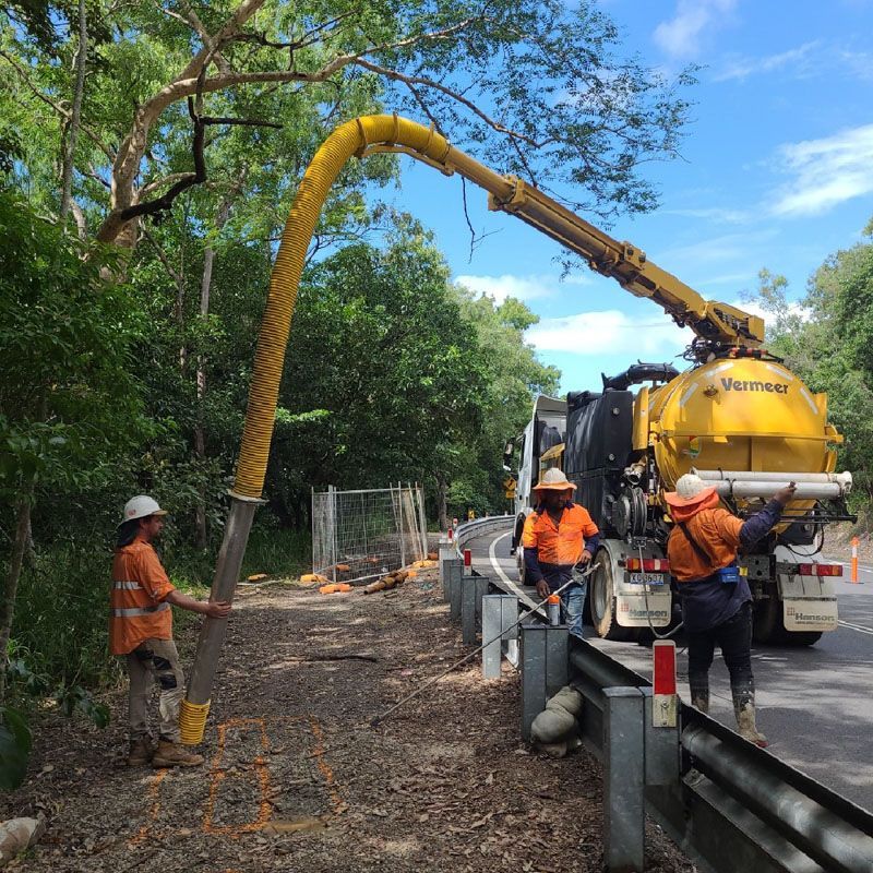 A group of construction workers are working on a road next to a vacuum truck