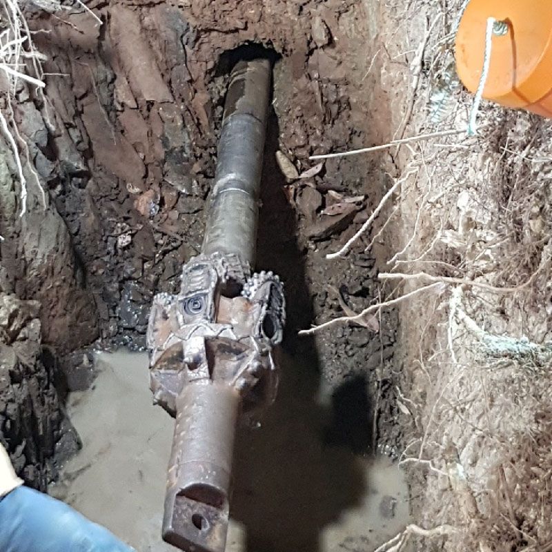 A person is working on a pipe in the dirt.