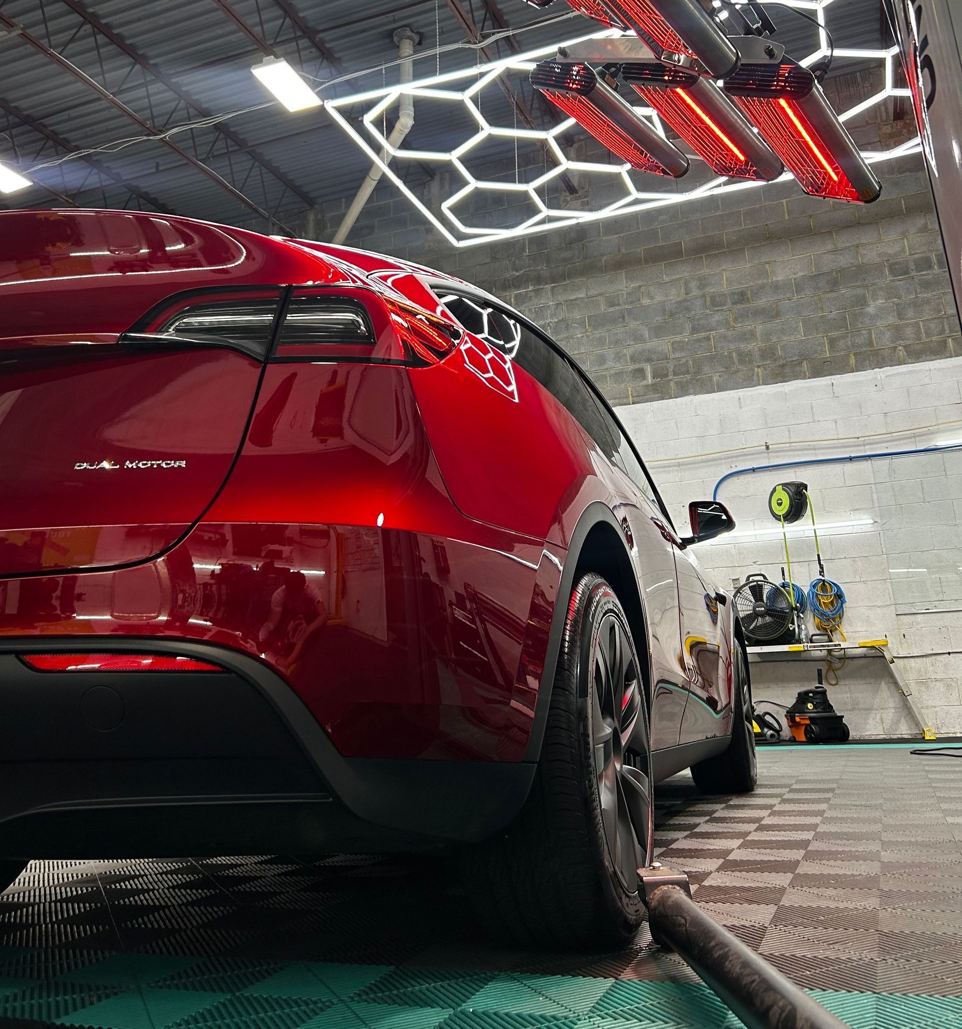 A red car is parked in a garage with a lot of lights on the ceiling.