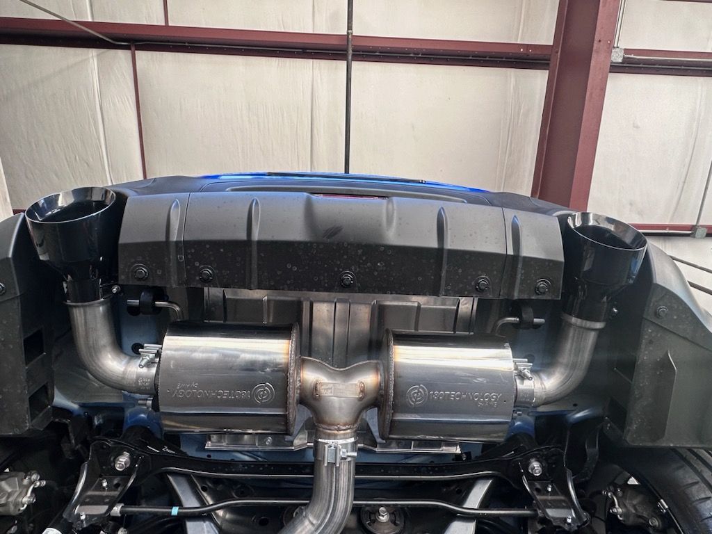 Underside view of a car showing a custom exhaust system with silver pipes and black exhaust tips.