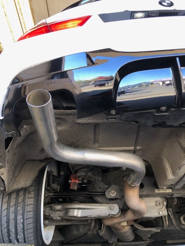 Underside of a white and black BMW with a custom exhaust pipe modification.