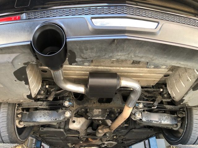 Underside of a black car, showing exhaust pipe and muffler. Steel and black components. Tires visible.