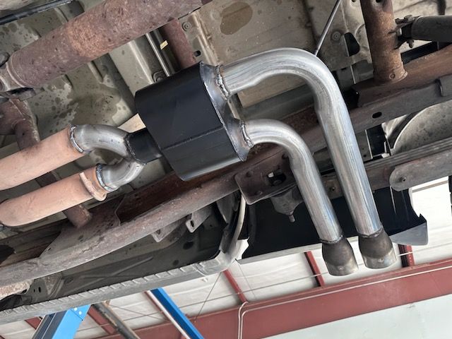 Undercarriage view of a vehicle exhaust system with a black muffler and polished pipes.