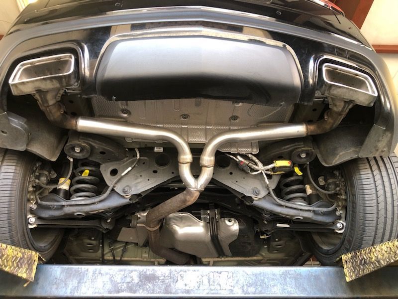 Undercarriage of a black car with dual exhaust pipes, viewed from below on a lift.