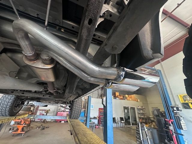 Underside view of a truck on a lift, showing a custom exhaust system with chrome tip.