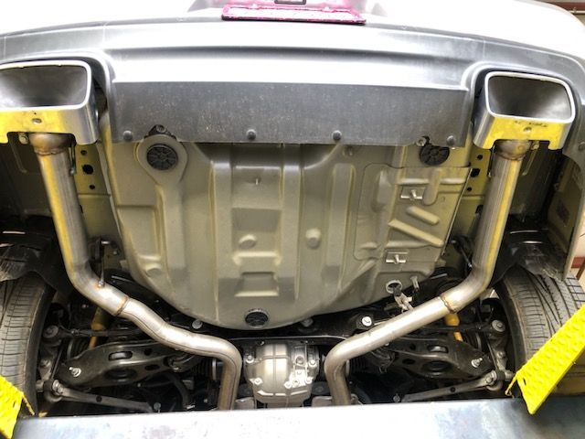 Underside view of a silver car showing its exhaust system with two square chrome exhaust tips.