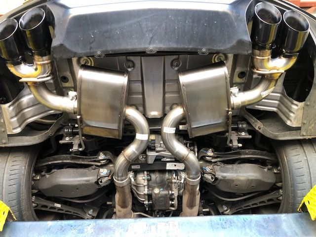 Undercarriage of a car with a custom exhaust system, showing silver pipes, black exhaust tips, and rectangular mufflers.