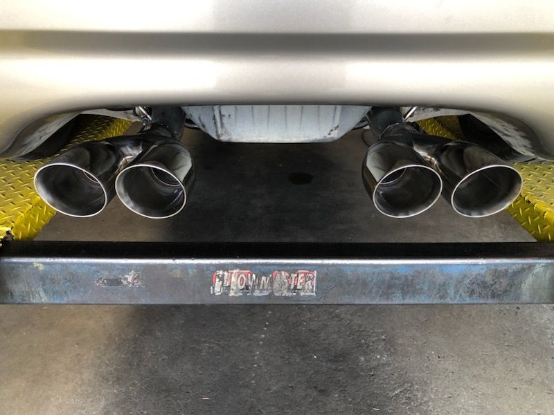 Close-up of a car's dual exhaust system with four polished tips, viewed from below, on a lift.