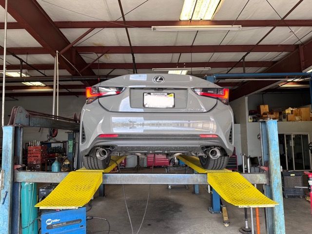 Gray Lexus RC coupe on a lift in a repair shop. Exhaust pipes visible.