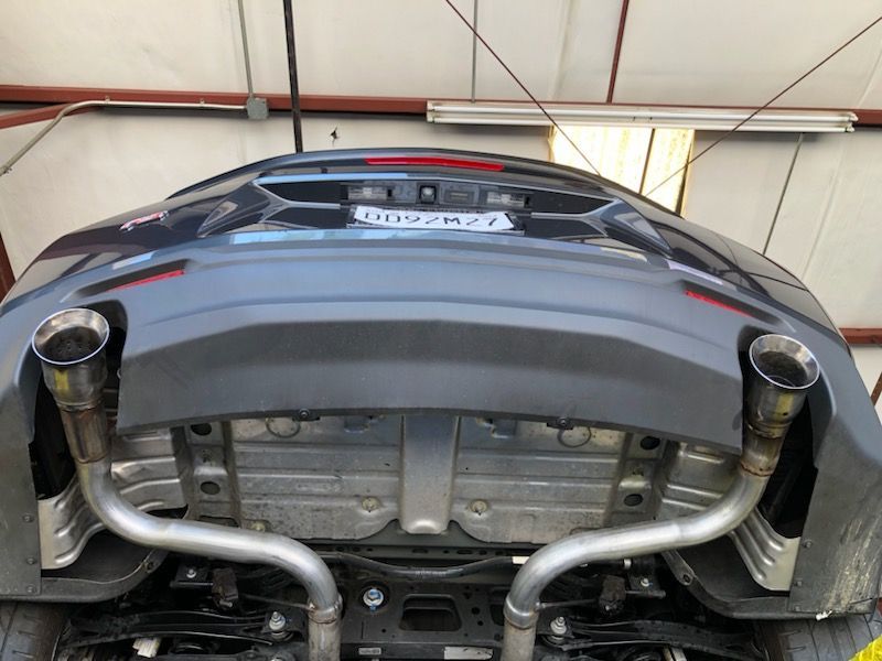 Underside of a gray car showing exhaust system with two chrome pipes.