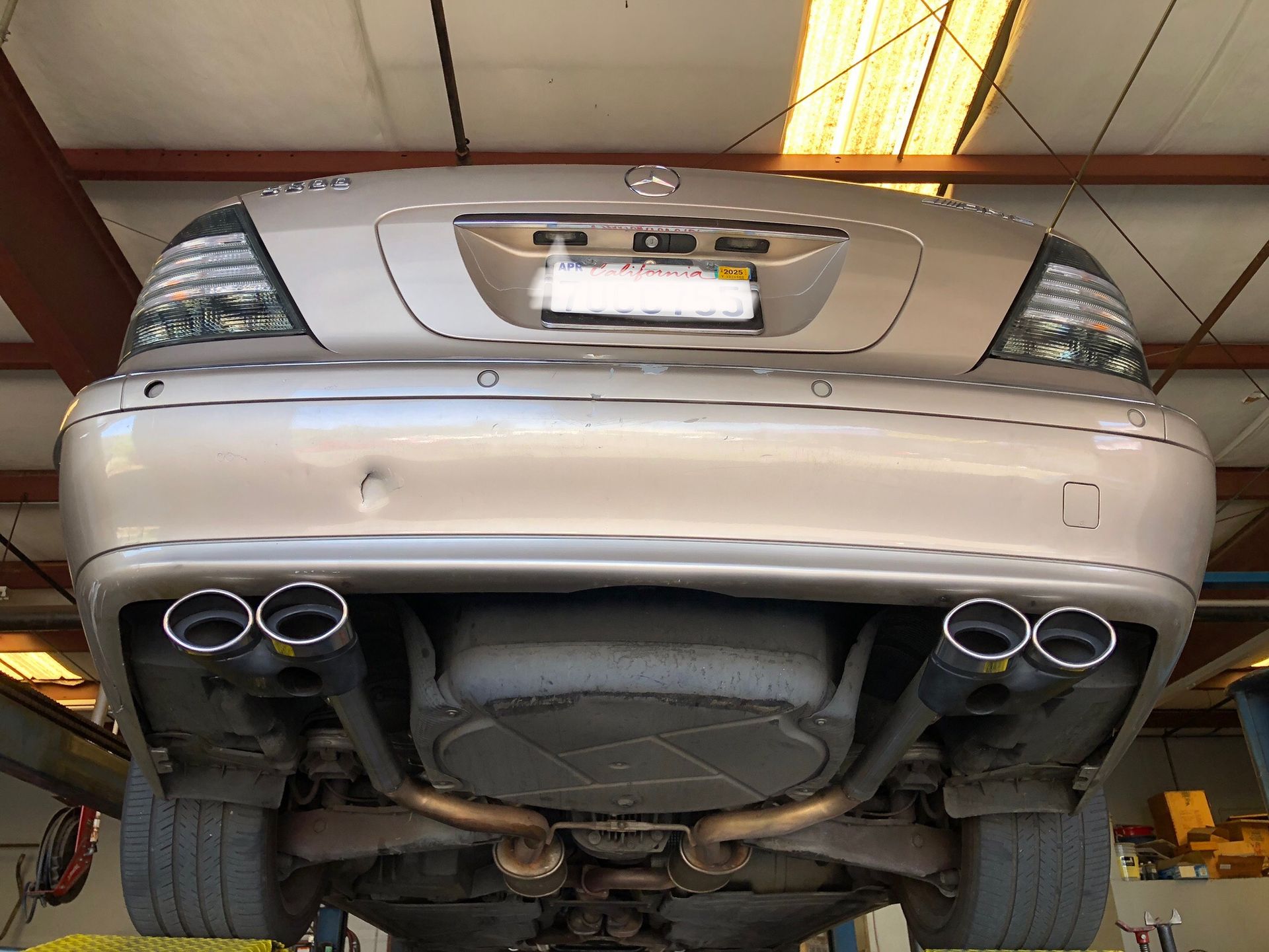 Tan Mercedes car on a lift, showing dual exhaust pipes.