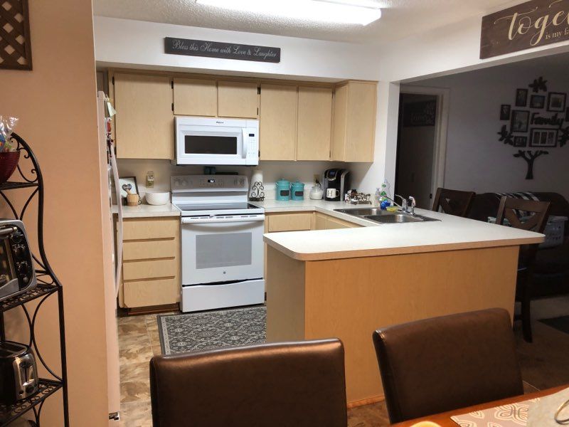 A kitchen with light wood cabinets, white appliances, and a peninsula counter leading into a dining area.
