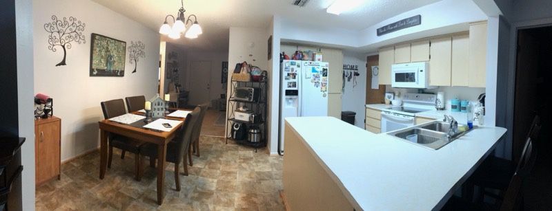 A panoramic view of an open-concept kitchen and dining area with a wooden table, light cabinets, and tiled floors.