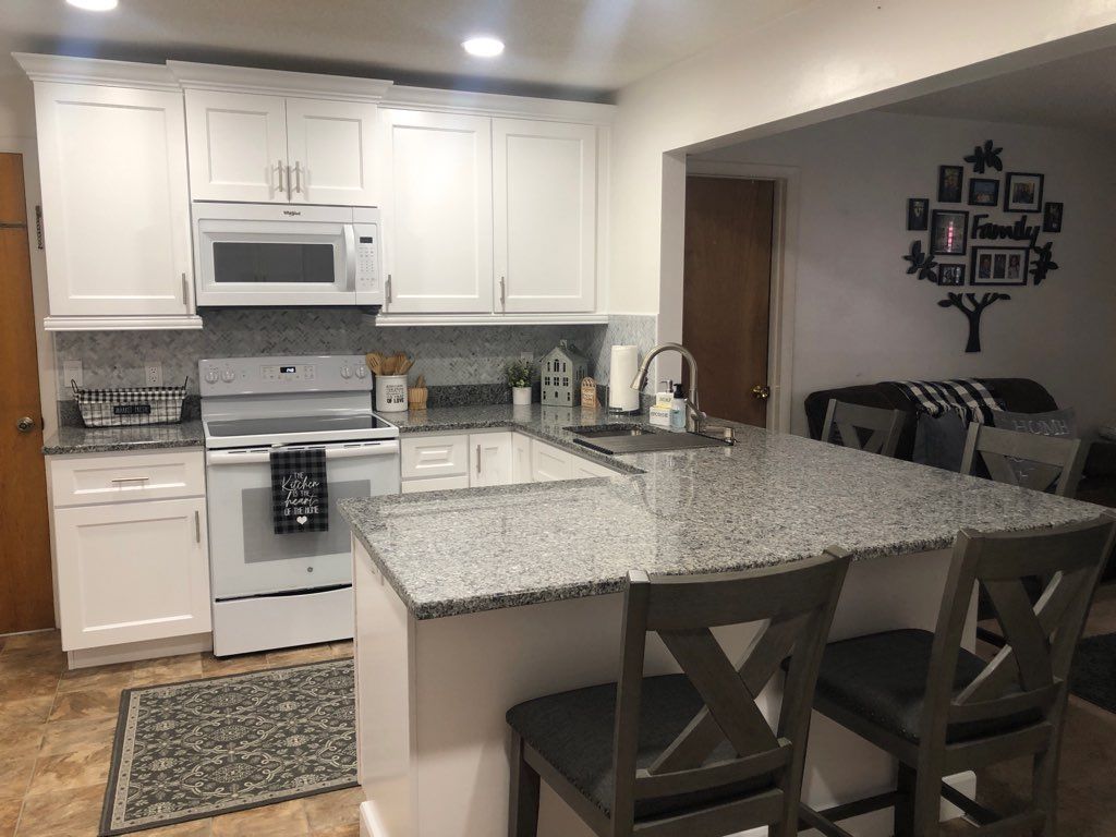A modern kitchen featuring white cabinets, granite countertops, a peninsula with two chairs, and a family tree wall decal.