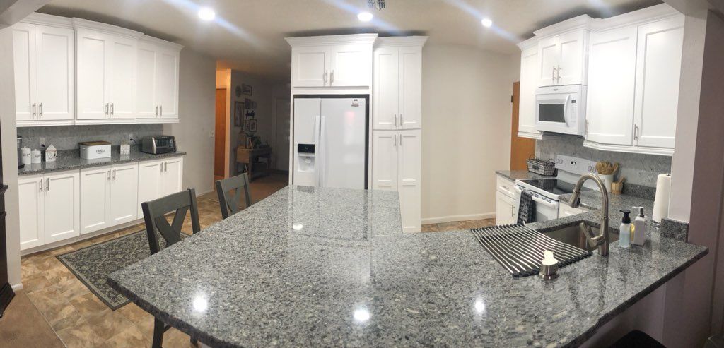 A bright, modern kitchen with white cabinets, a large granite island, stainless steel appliances, and a gray rug.
