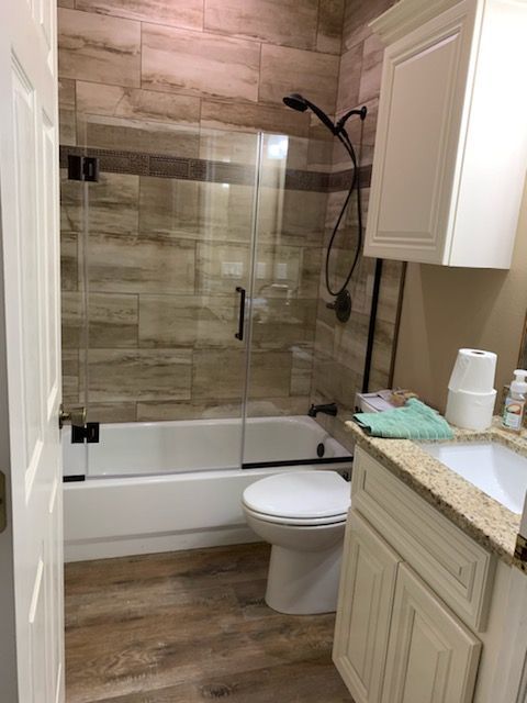 A bathroom featuring a shower with wood-look tile, and a vanity with a light-colored countertop.