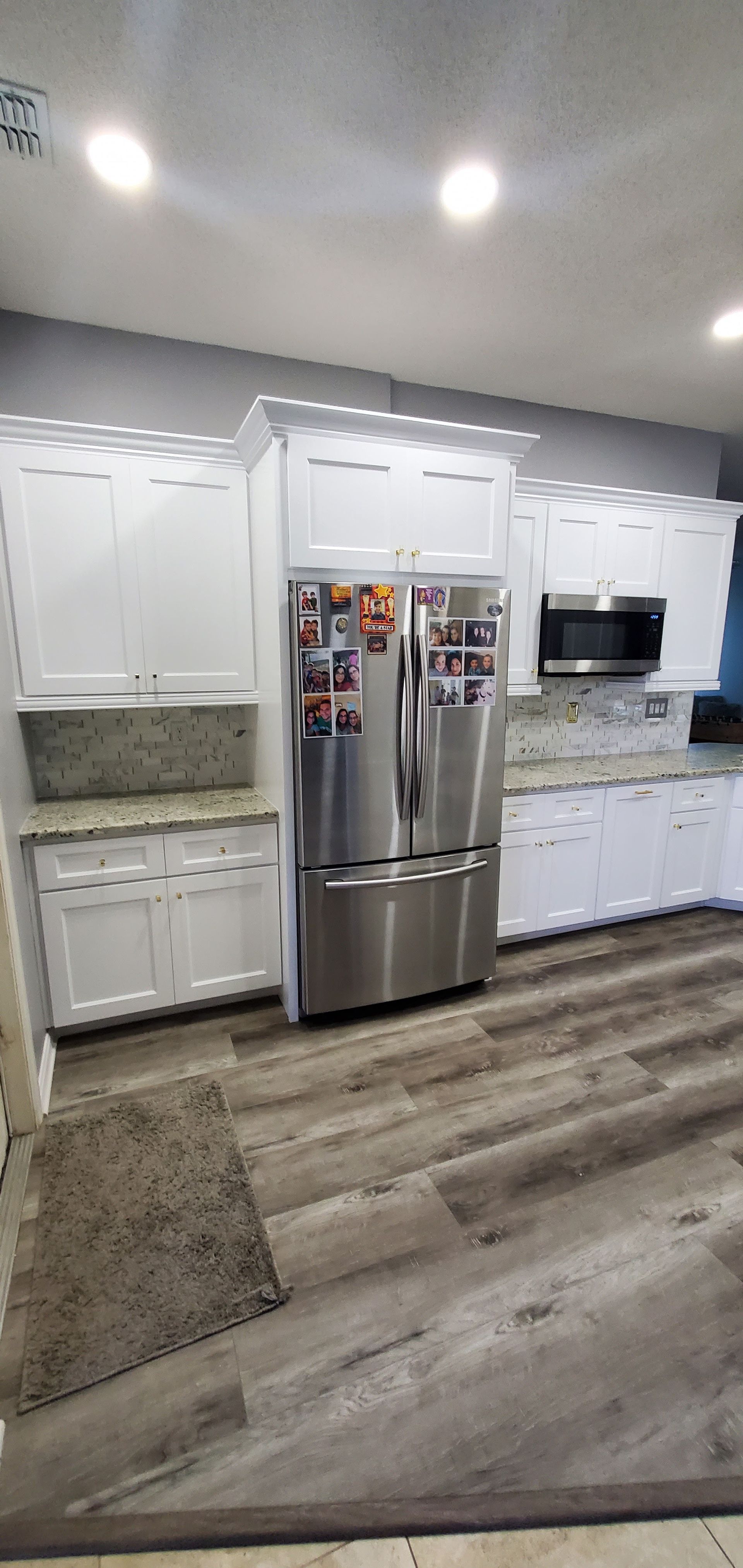 A modern kitchen featuring white cabinets, stainless steel appliances, speckled stone countertops, and gray wood flooring.
