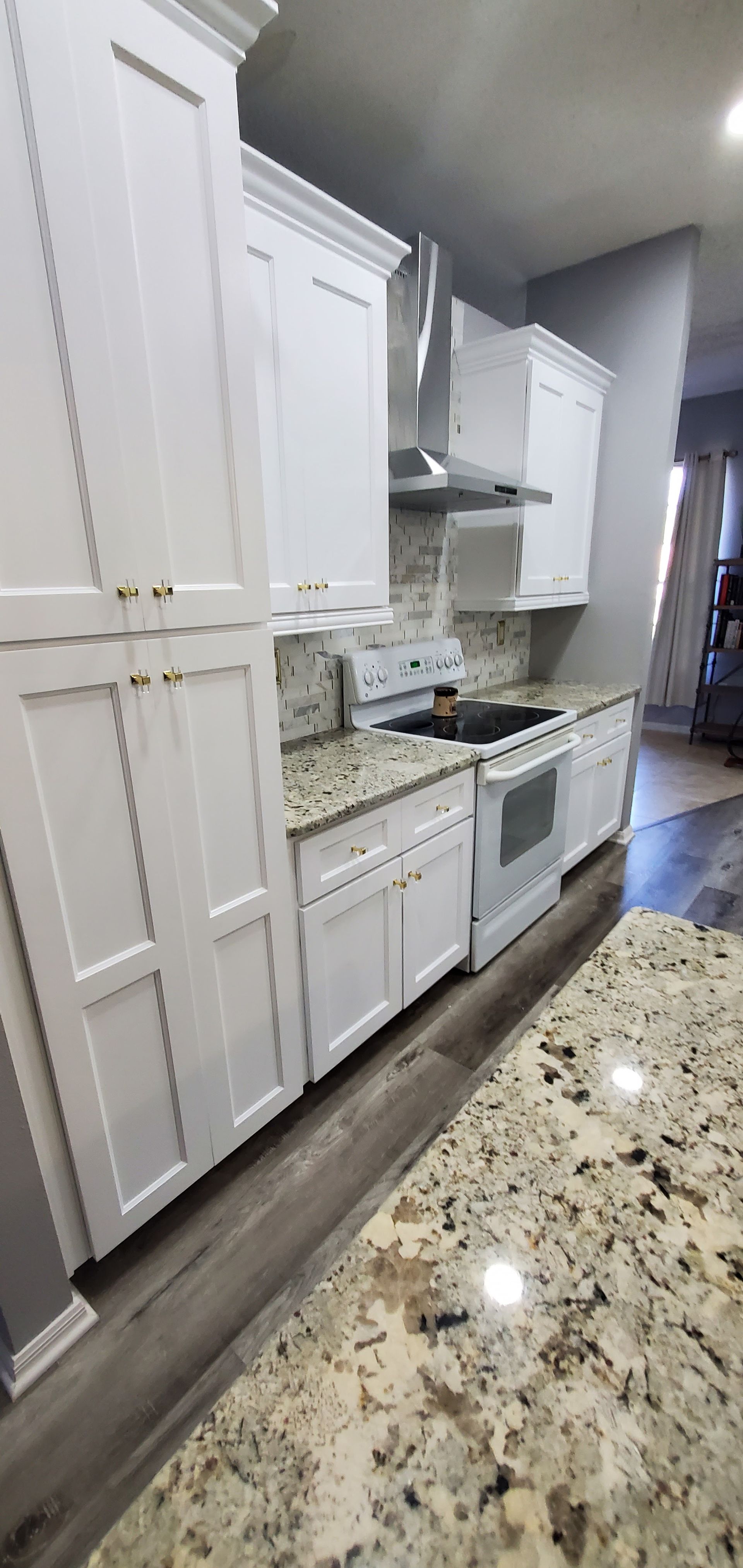 Modern white kitchen with granite countertops, stainless steel appliances, and wood-look flooring.