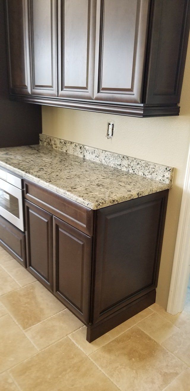 Dark wooden kitchen cabinets with speckled granite countertops and light-colored tile floors.