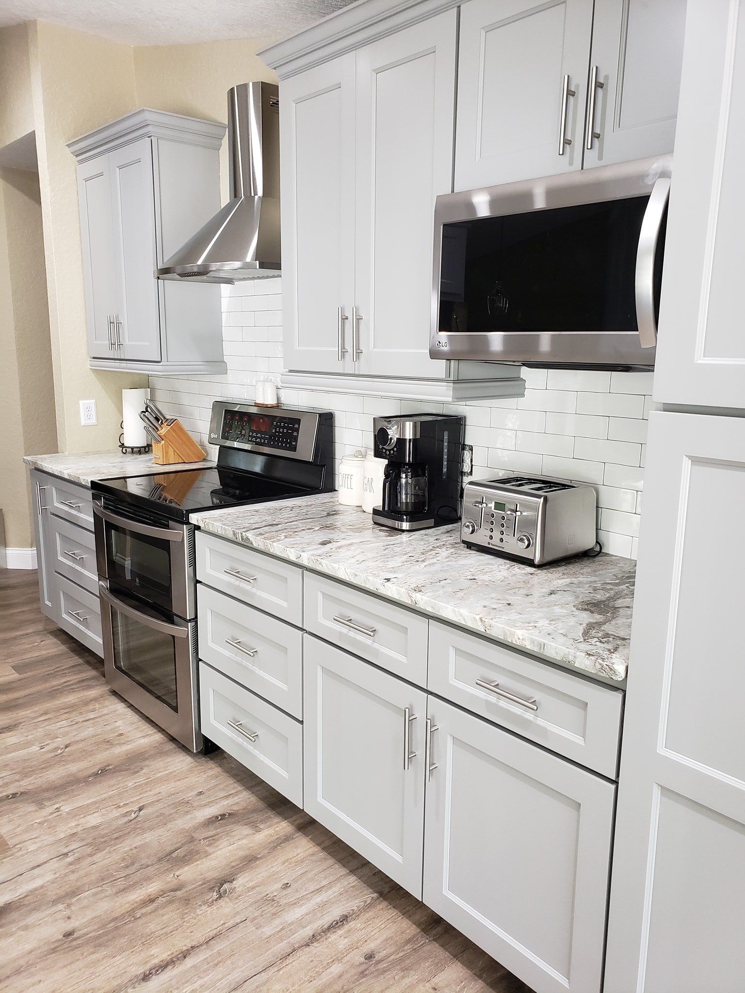 A modern kitchen with light gray cabinetry, stainless steel appliances, and a marble-patterned countertop.