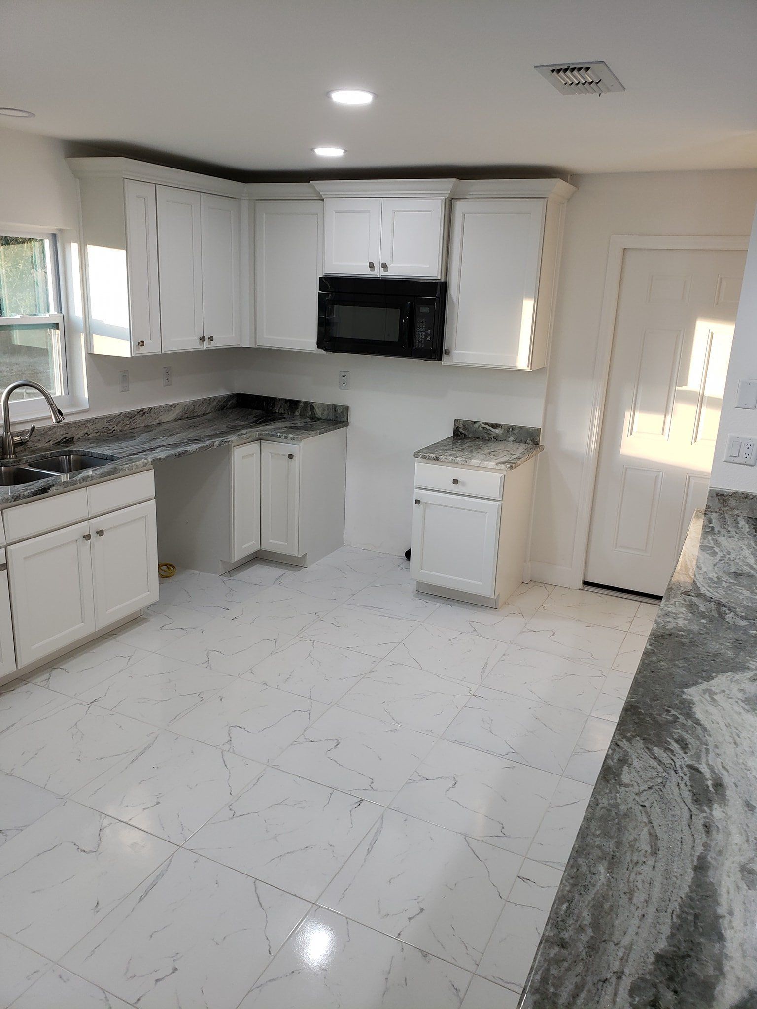 A bright kitchen featuring white cabinets, granite countertops, tile floors, and a built-in microwave.