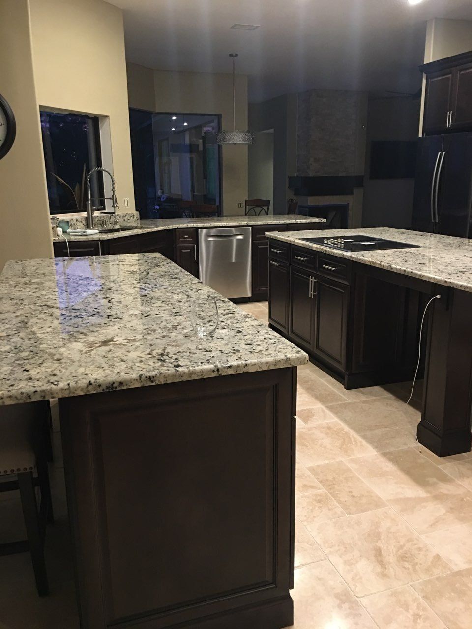 A spacious kitchen featuring dark wood cabinets, speckled granite countertops, a center island, and tiled flooring.