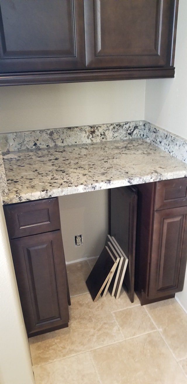 A small kitchen desk area with dark wood cabinets, a speckled granite countertop, and floor tiles.