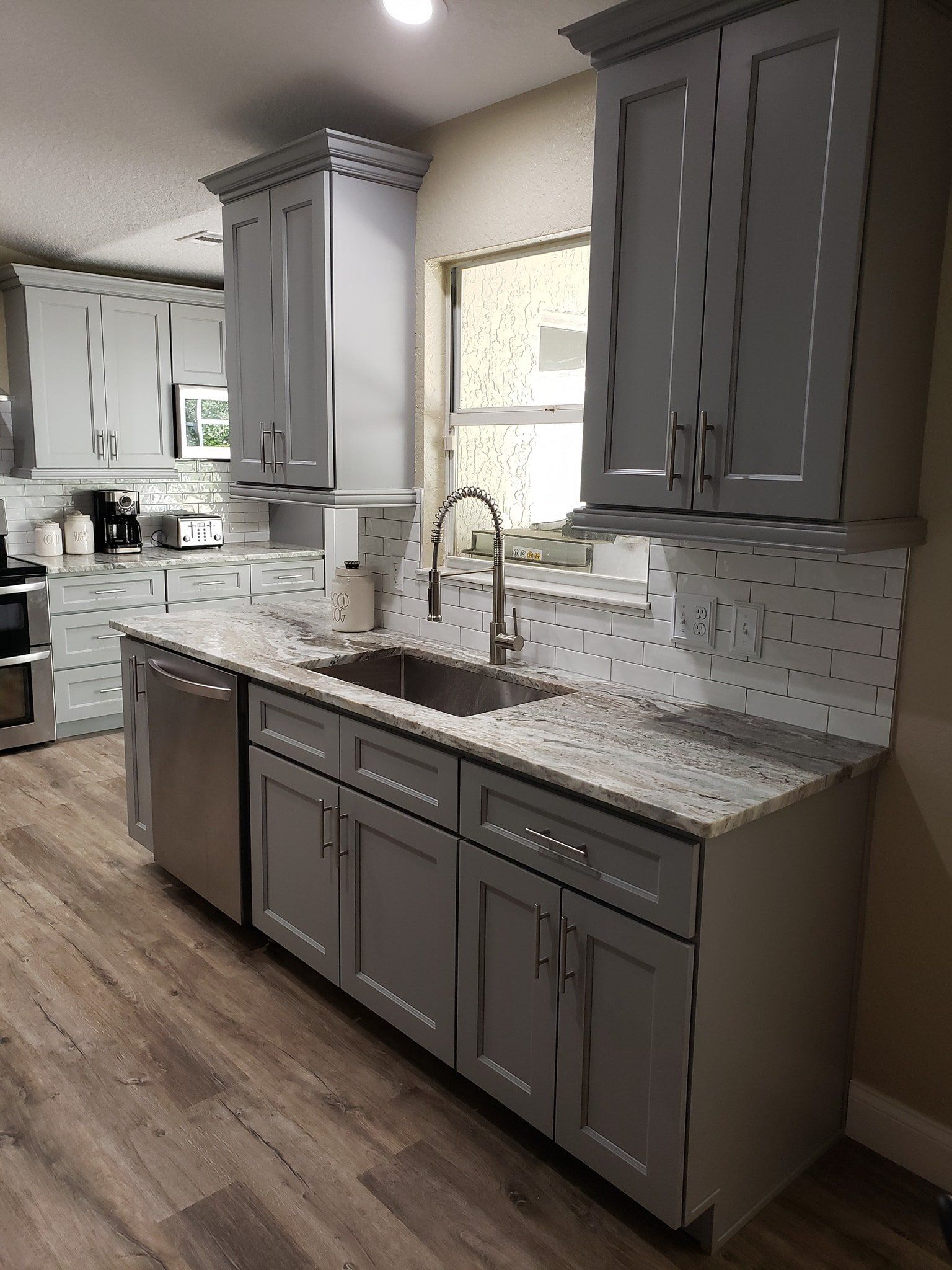Modern kitchen with gray cabinets, speckled granite countertops, stainless steel appliances, and wood-look flooring.