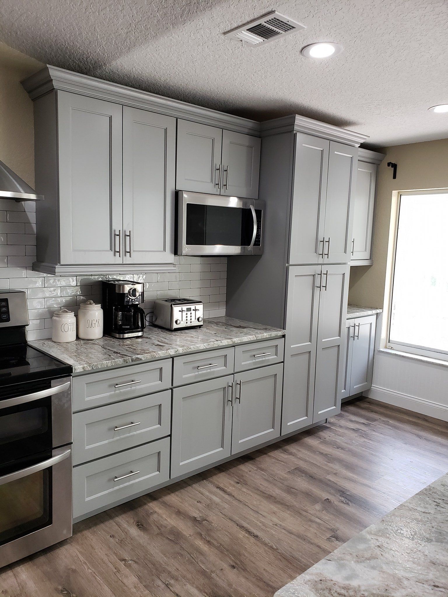 Modern kitchen with grey cabinets, stainless steel appliances, granite countertops, and light wood-look flooring.